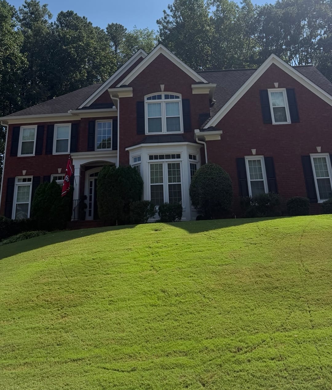 A red brick two-storey home on a green lawn after a KM Property Restorations exterior clean