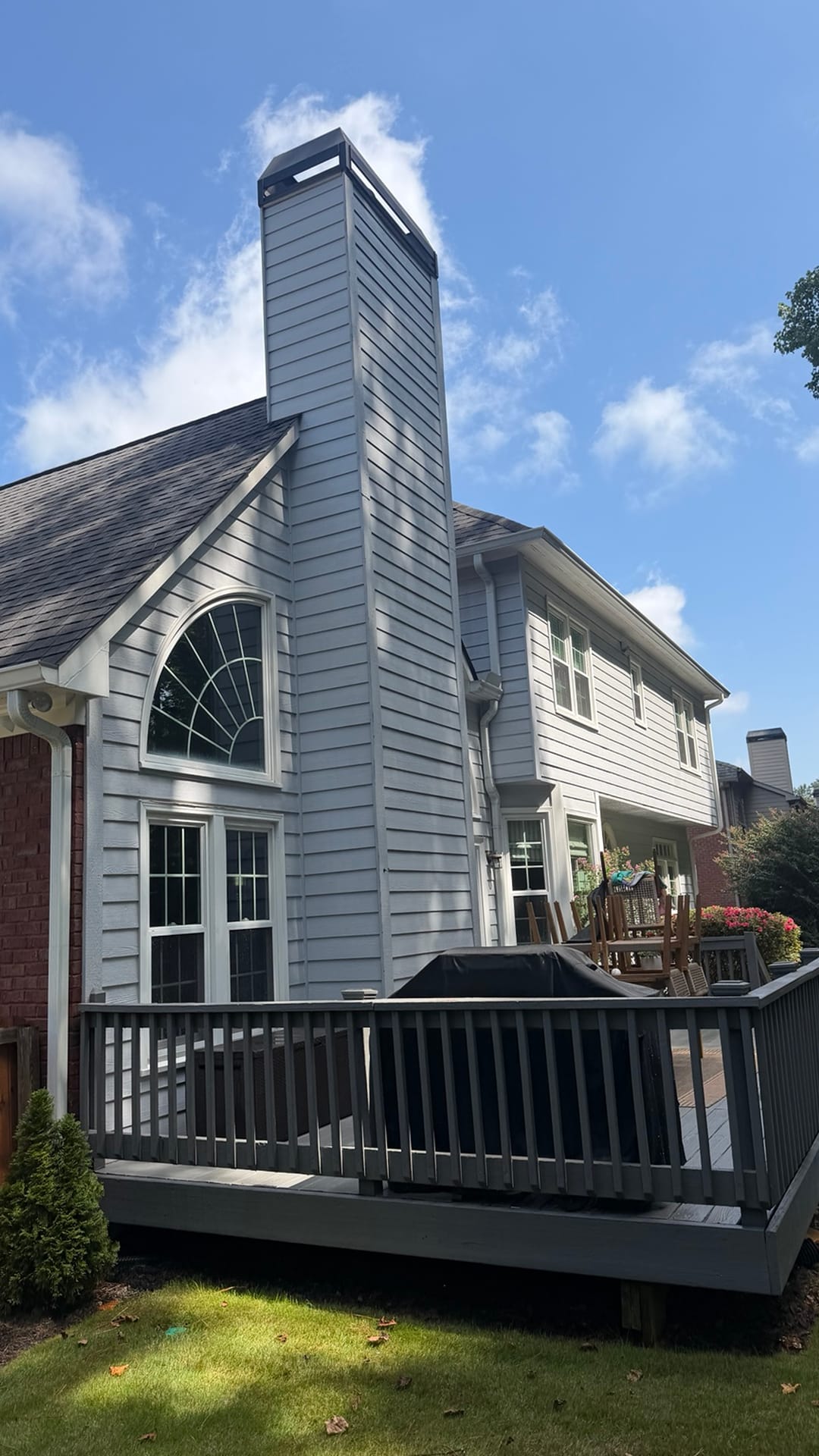 The back of a grey two-storey home with a tall chimney and a wood deck, siding freshly washed by KM Property Restorations