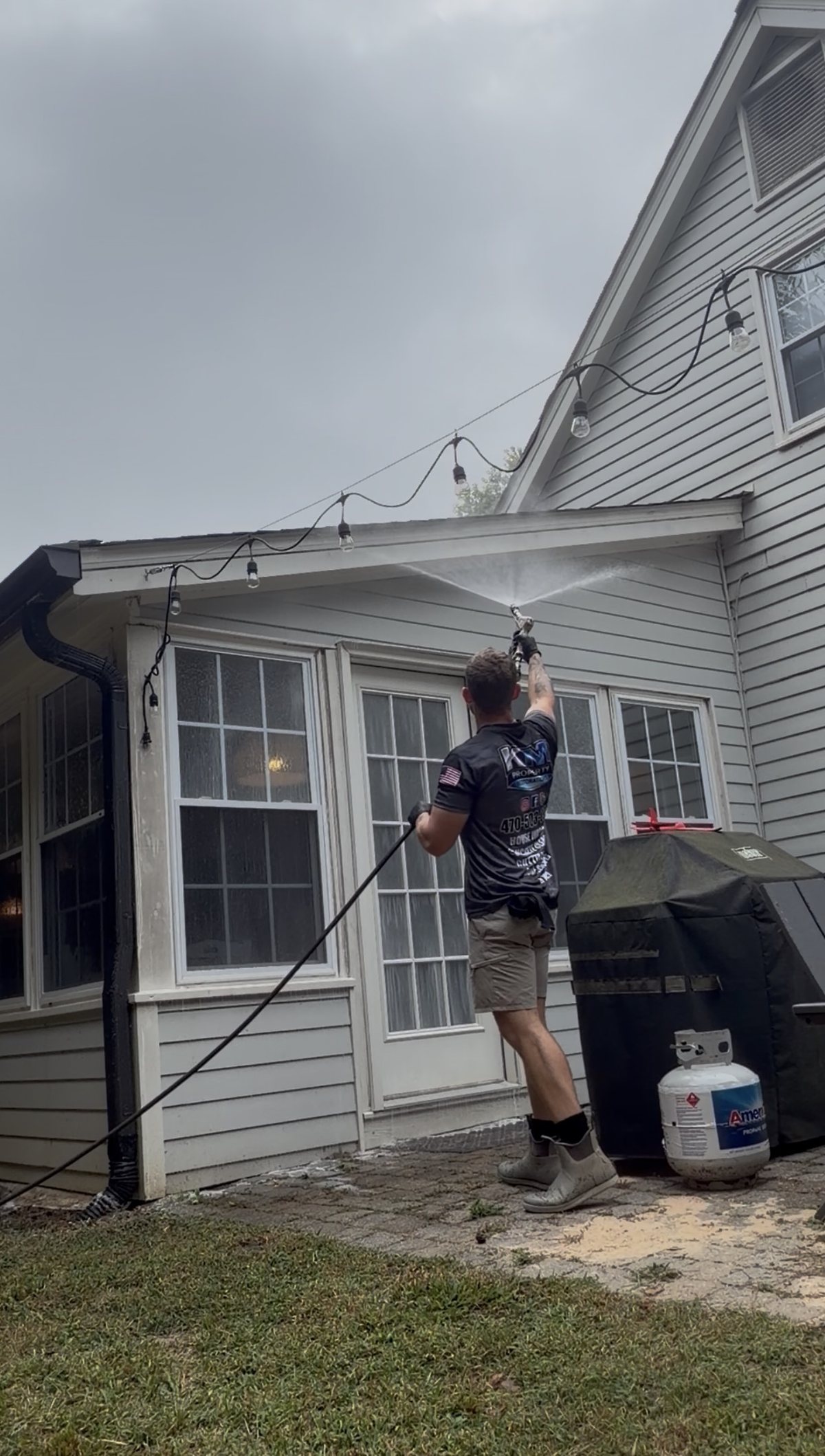 Kevin of KM Property Restorations soft washing the eaves and siding above a back patio