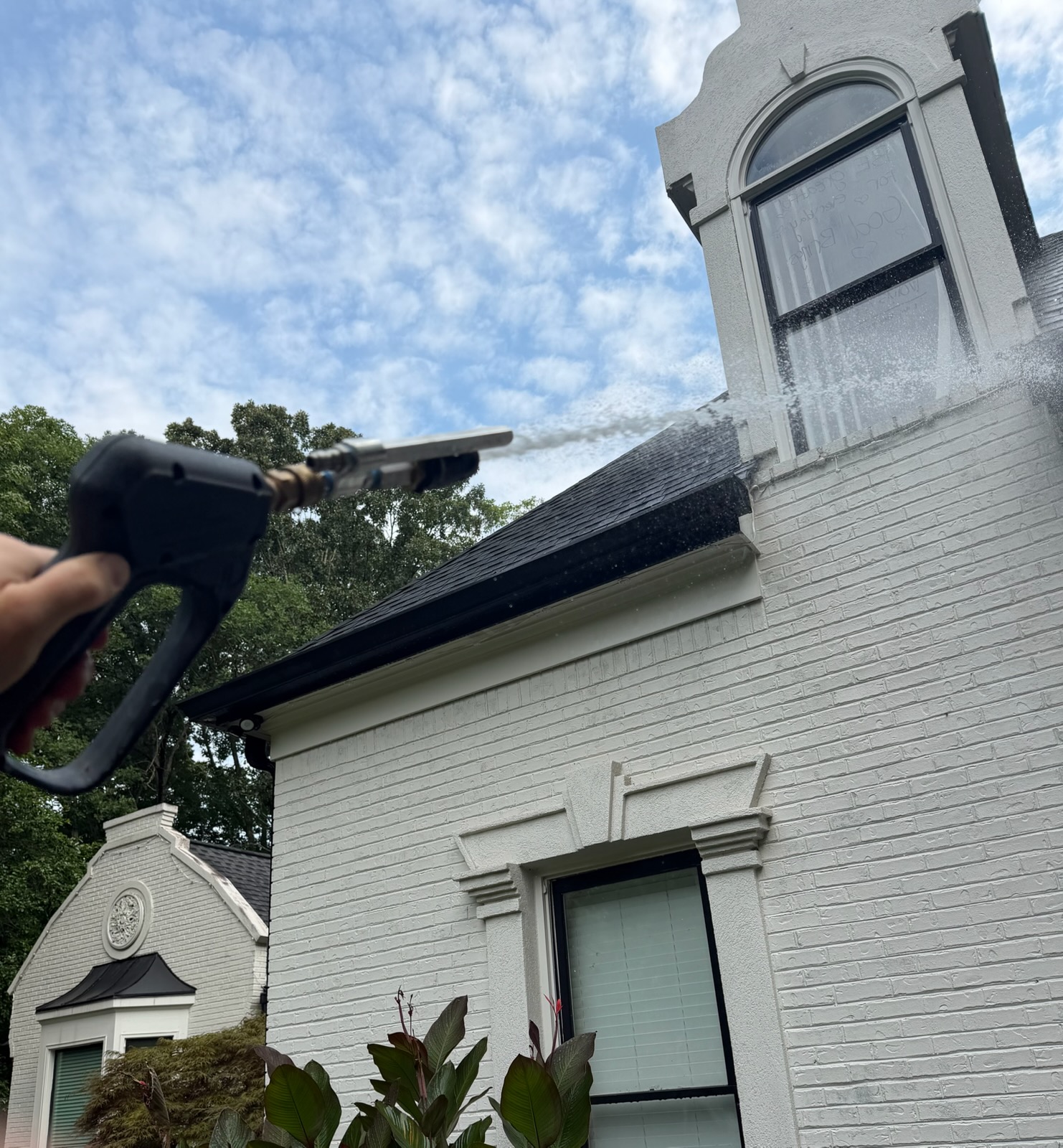 A KM Property Restorations pressure washer wand rinsing the upper brick and dormer of a white Atlanta home